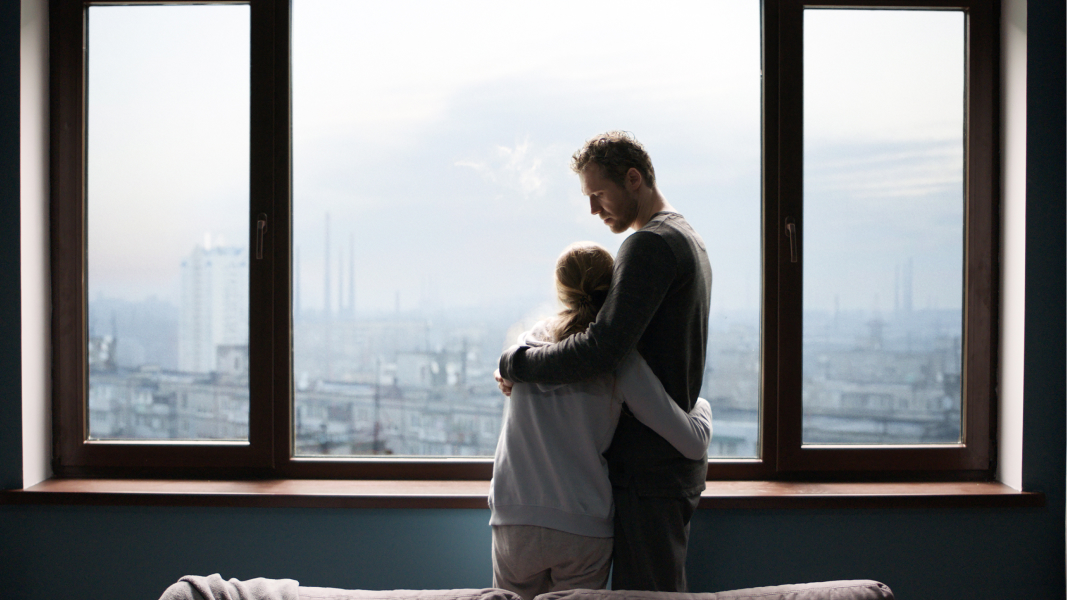 A couple hugging in front of a window with a skyline view